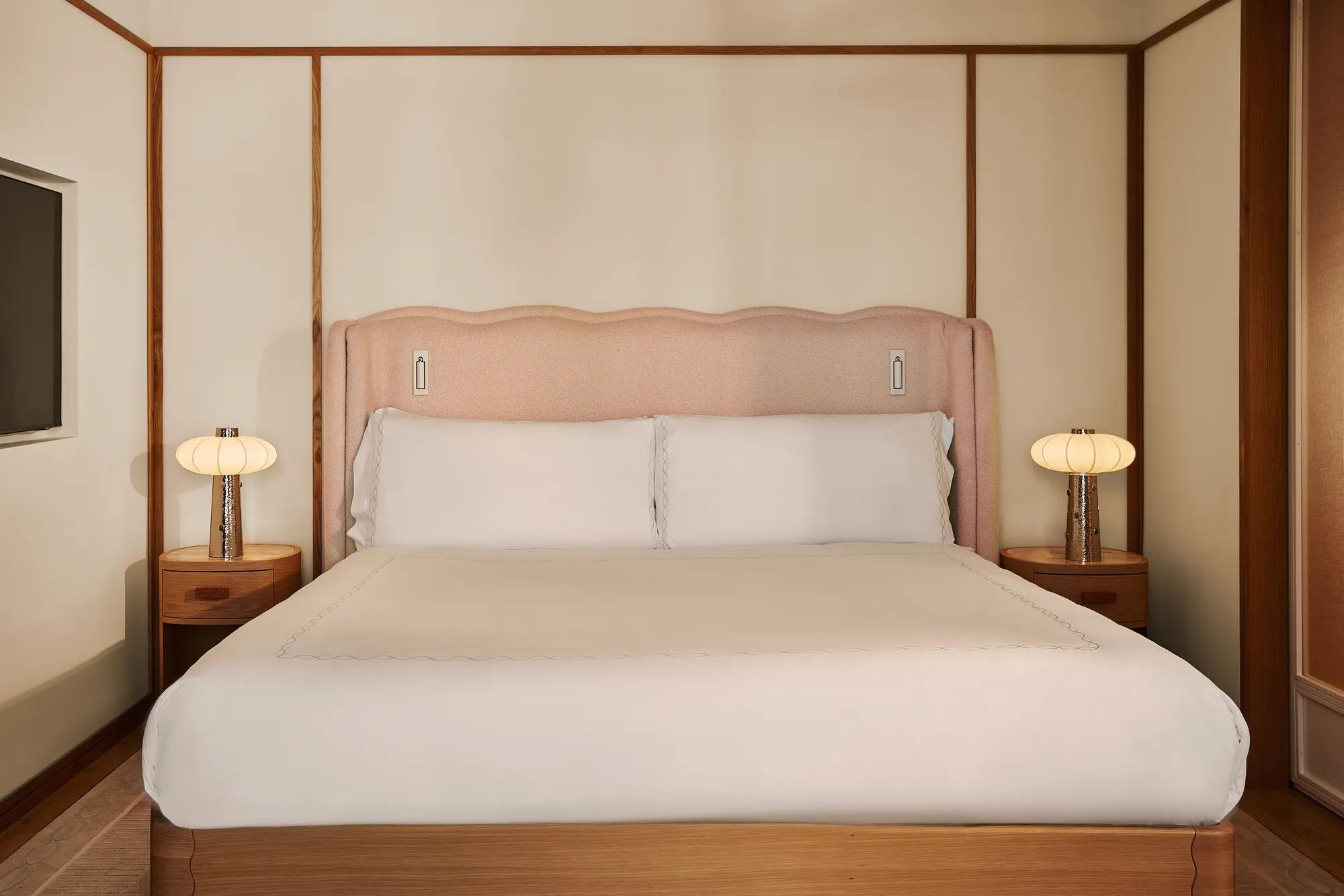 King bed with upholstered pink headboard, white linens, wooden bedside tables with lamps, and paneled walls.