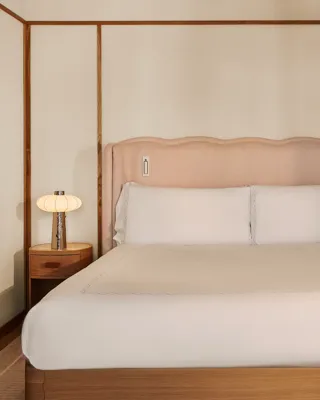 King bed with upholstered pink headboard, white linens, wooden bedside tables with lamps, and paneled walls.