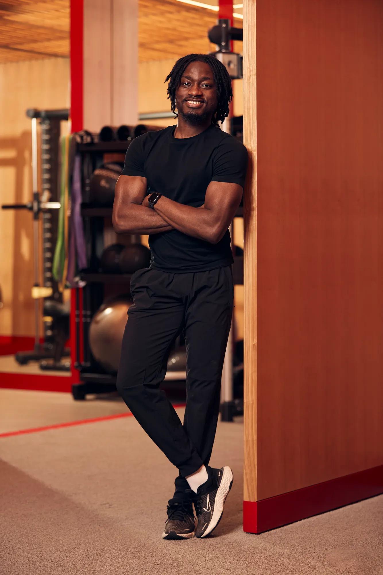An image of a personal training wearing gym clothes leans against a wooden wall