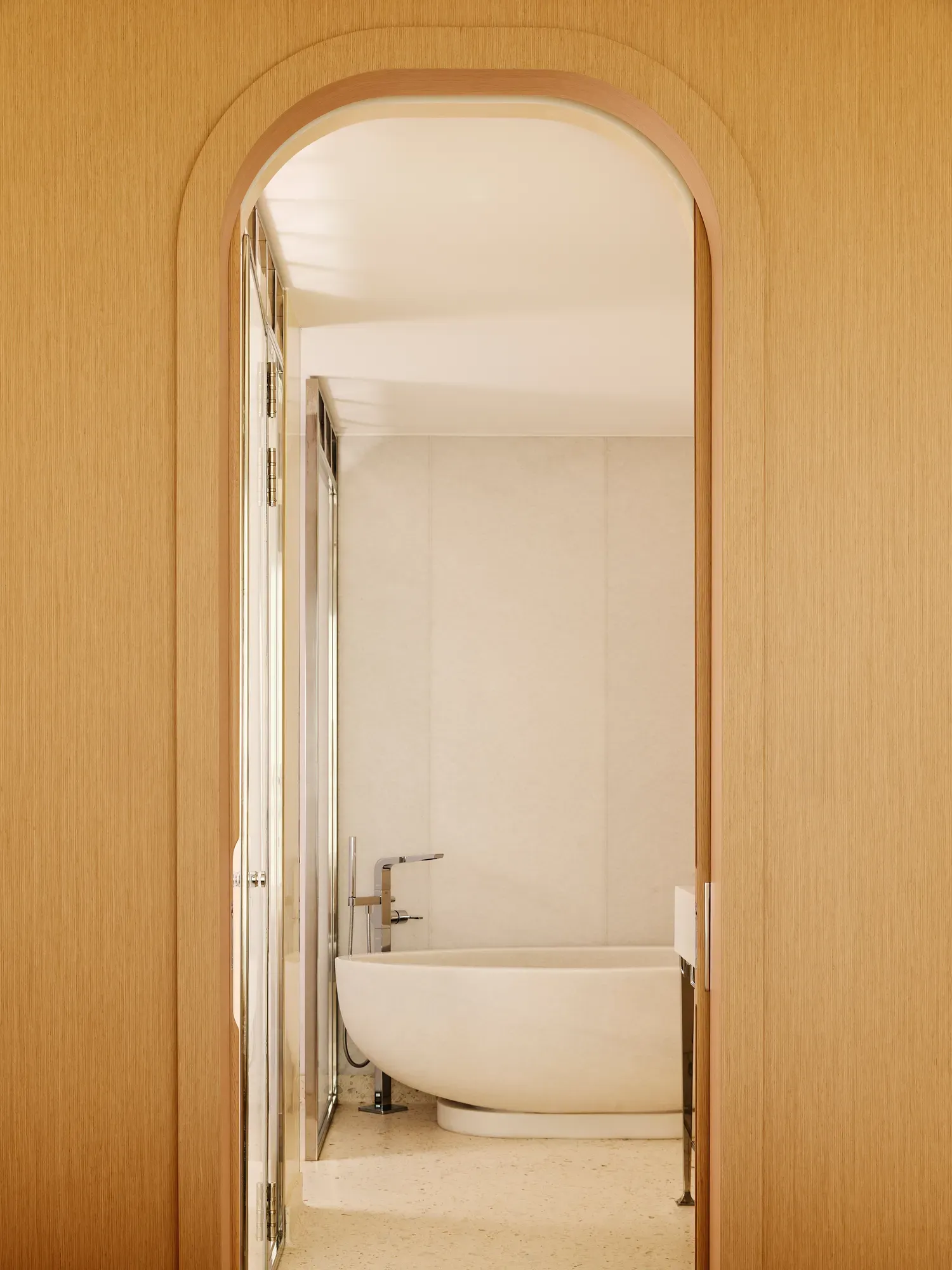 Salle de bain minimaliste avec baignoire ovale autoportante, vue à travers une porte arquée en bois.