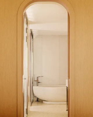Salle de bain minimaliste avec baignoire ovale autoportante, vue à travers une porte arquée en bois.