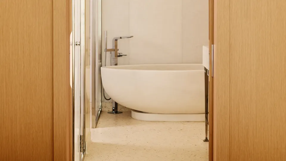 Salle de bain minimaliste avec baignoire ovale autoportante, vue à travers une porte arquée en bois.