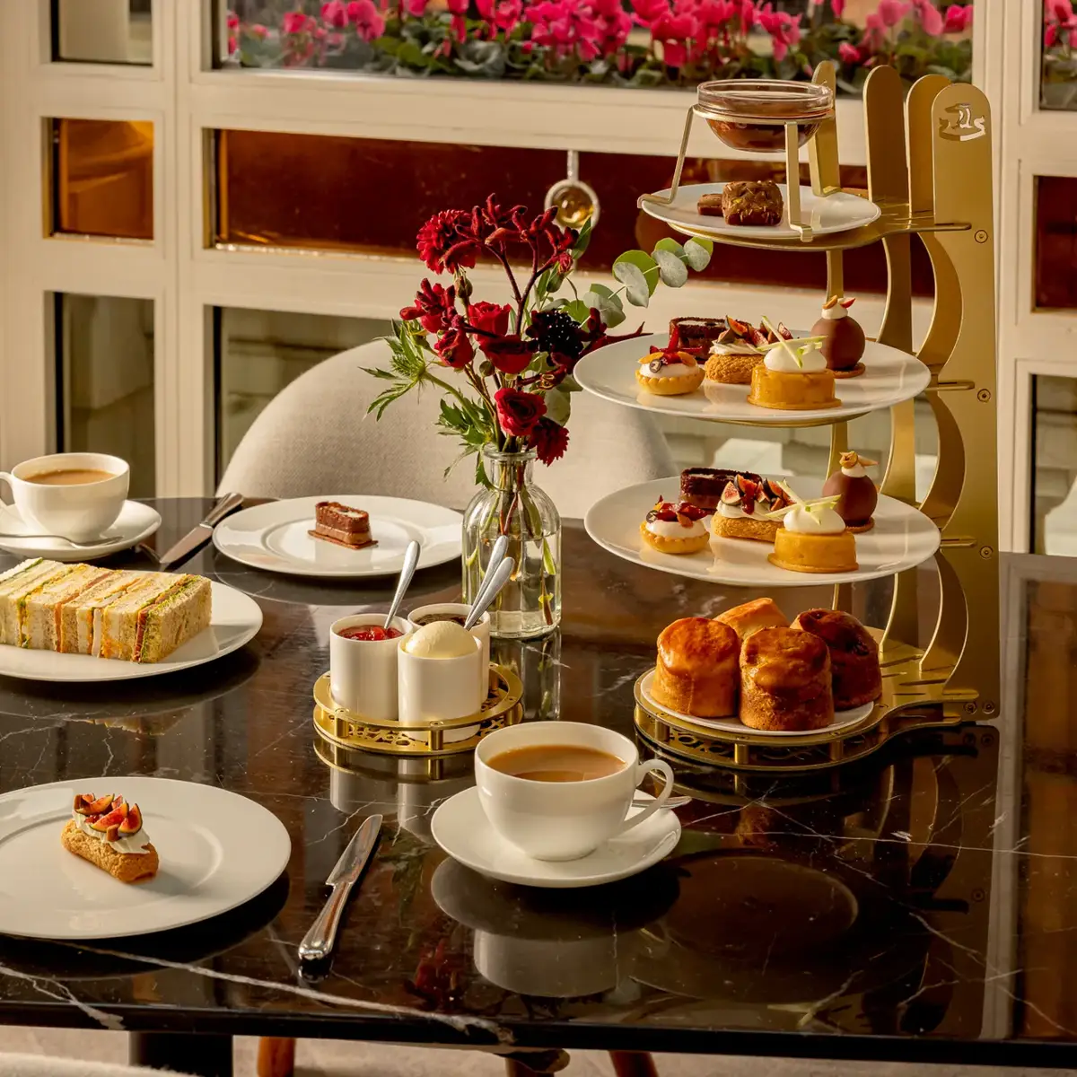 Afternoon tea spread with sandwiches, scones, pastries, and cups of tea arranged on a black marble table beside a multi-tiered stand.