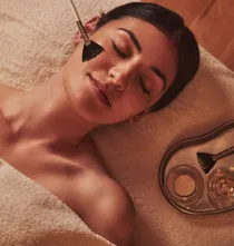 Spa therapist applying a facial treatment with a soft brush to a woman lying relaxed on a towel.