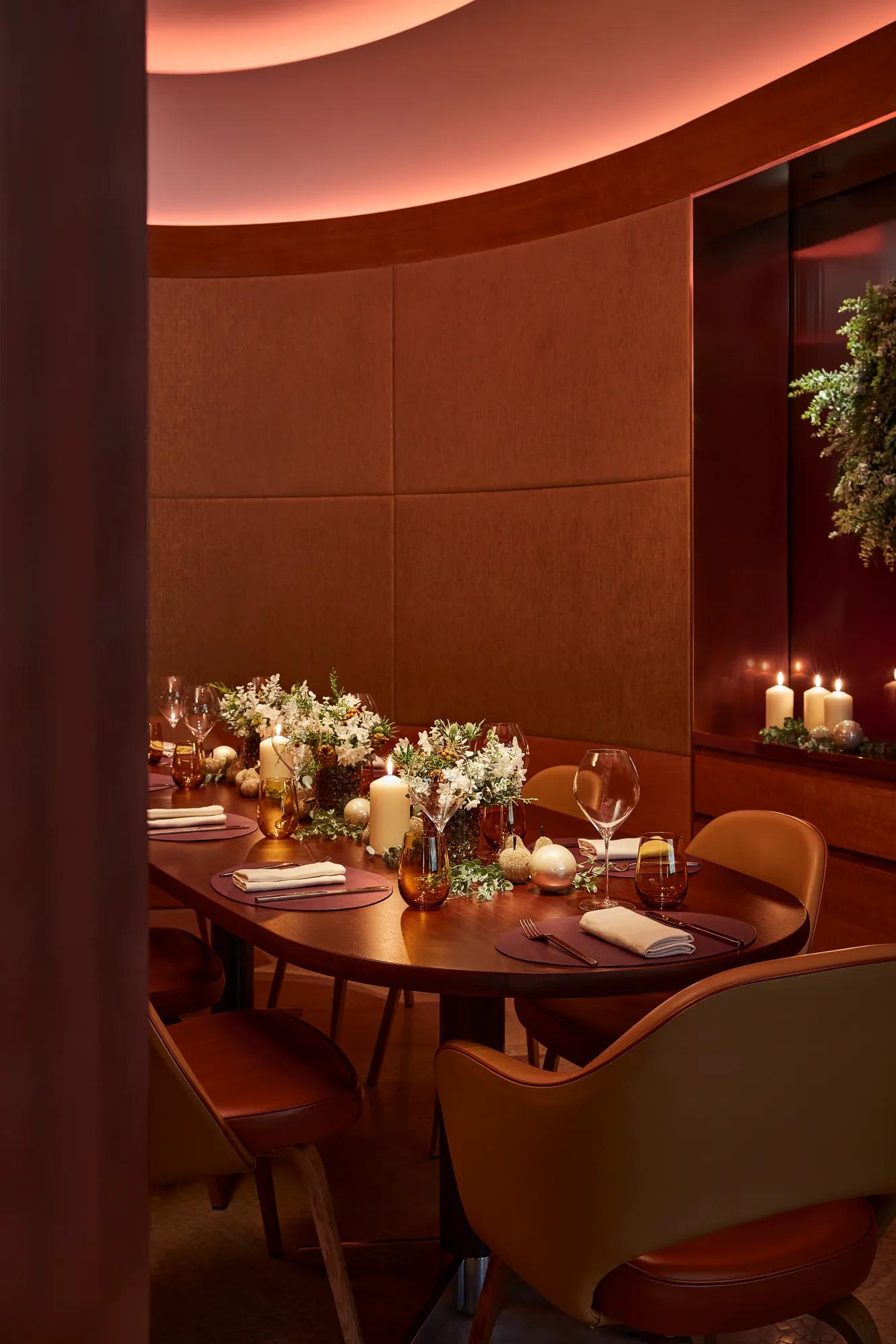 Intimate dining table set with flowers, candles, and glassware in a warm, softly lit private dining room.
