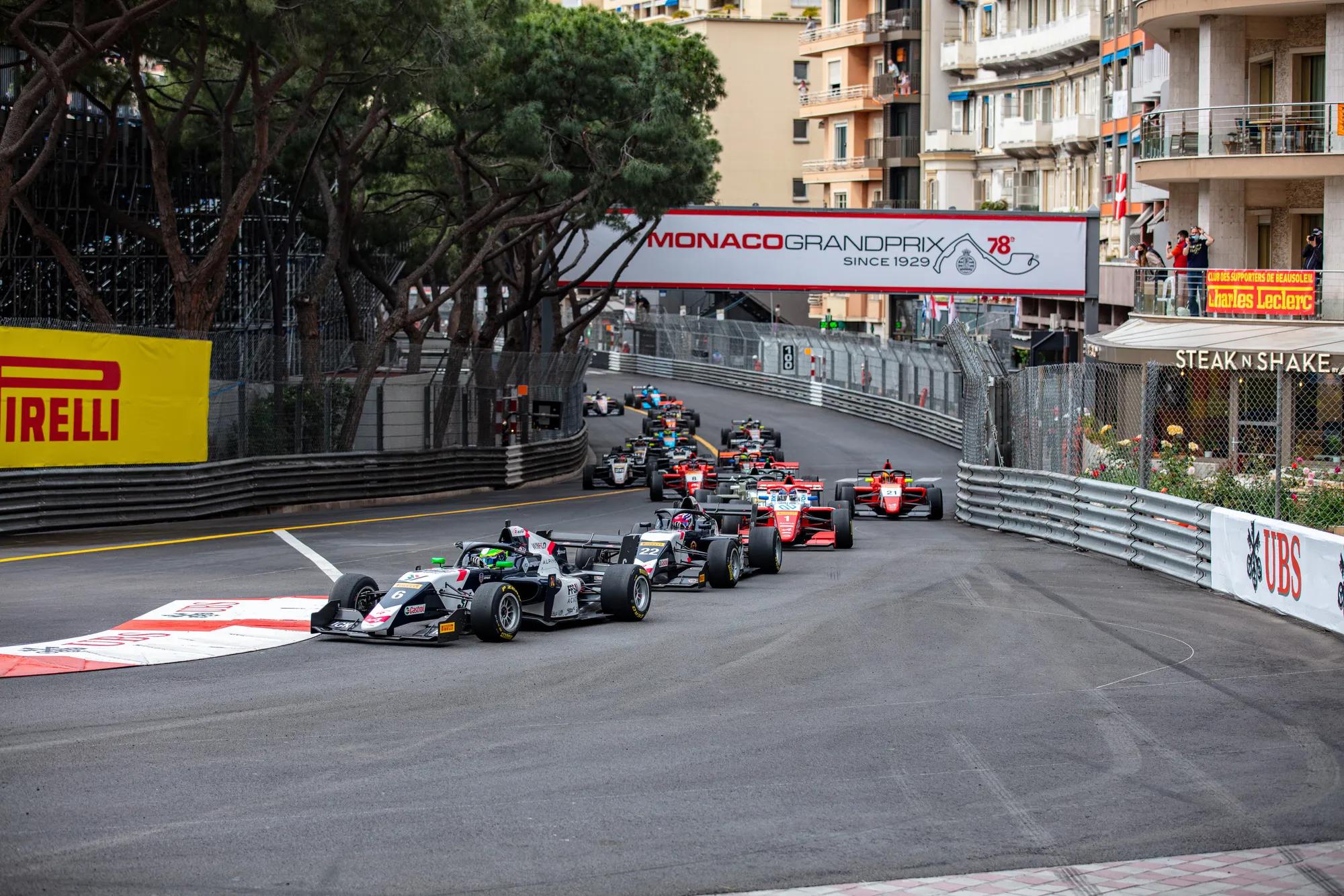 Race cars navigating Monaco Grand Prix street circuit, lined with barriers, grandstands, and city buildings