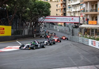 Race cars navigating Monaco Grand Prix street circuit, lined with barriers, grandstands, and city buildings