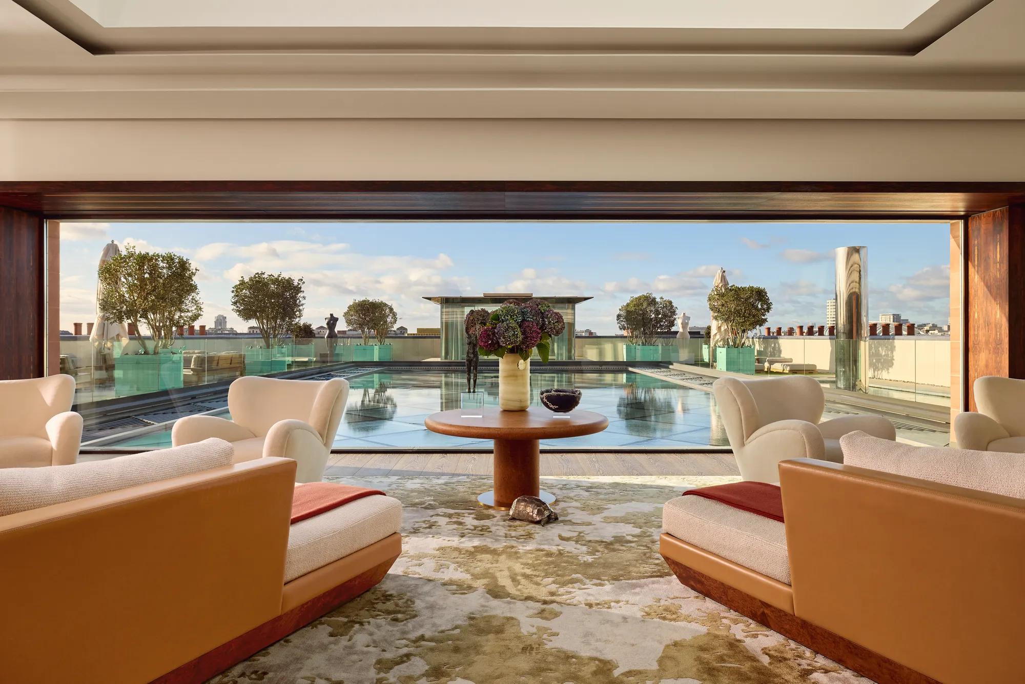 Lounge with cream armchairs opening onto a rooftop terrace with a reflective pool and city views.