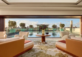 Lounge with cream armchairs opening onto a rooftop terrace with a reflective pool and city views.