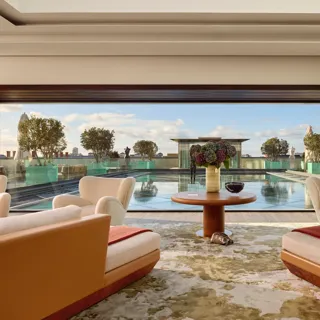 Lounge with cream armchairs opening onto a rooftop terrace with a reflective pool and city views.