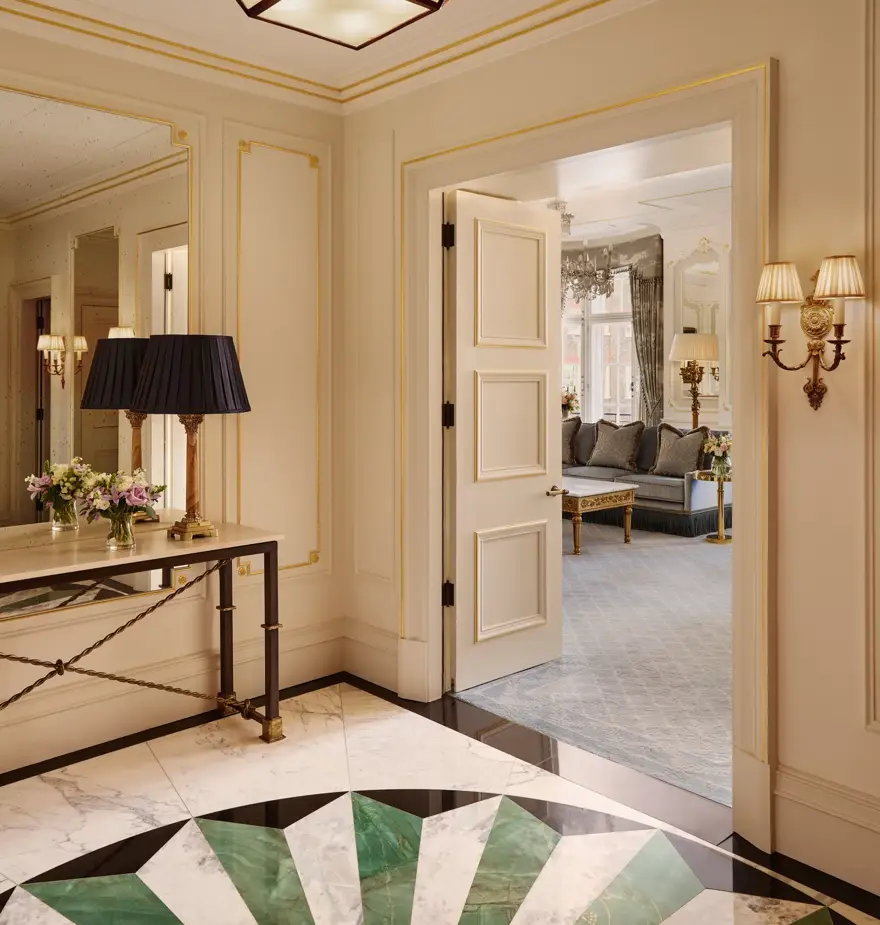 Elegant suite entry with marble floor, console table and open doors leading to a bright living room with sofas.