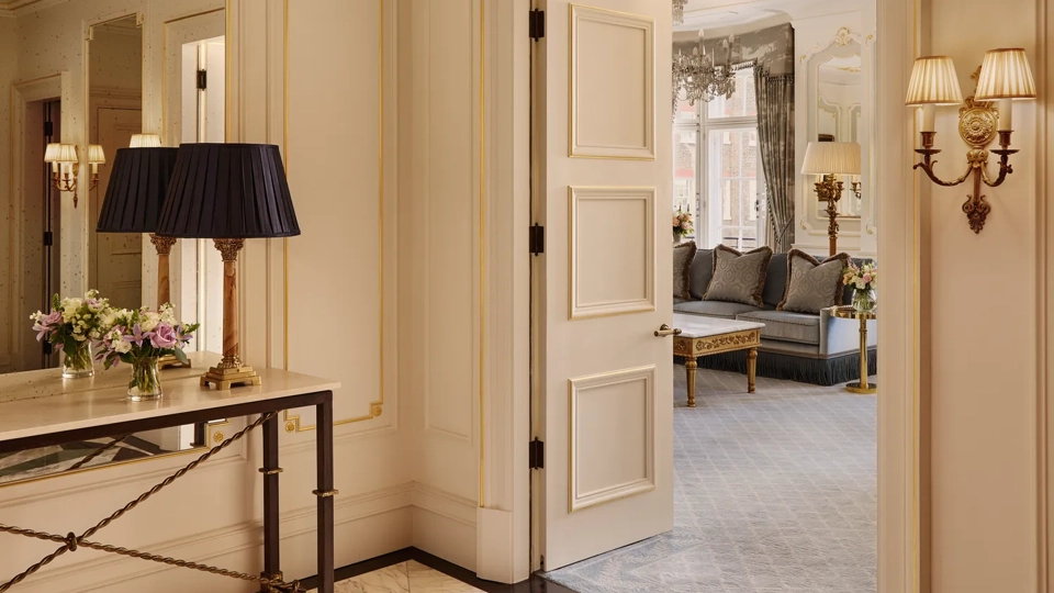 Elegant suite entry with marble floor, console table and open doors leading to a bright living room with sofas.