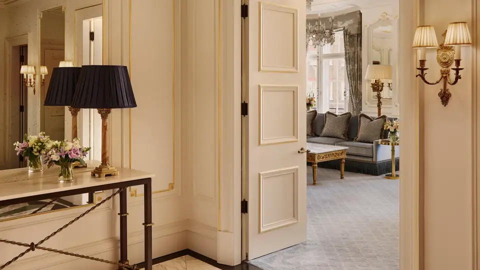 Elegant suite entry with marble floor, console table and open doors leading to a bright living room with sofas.