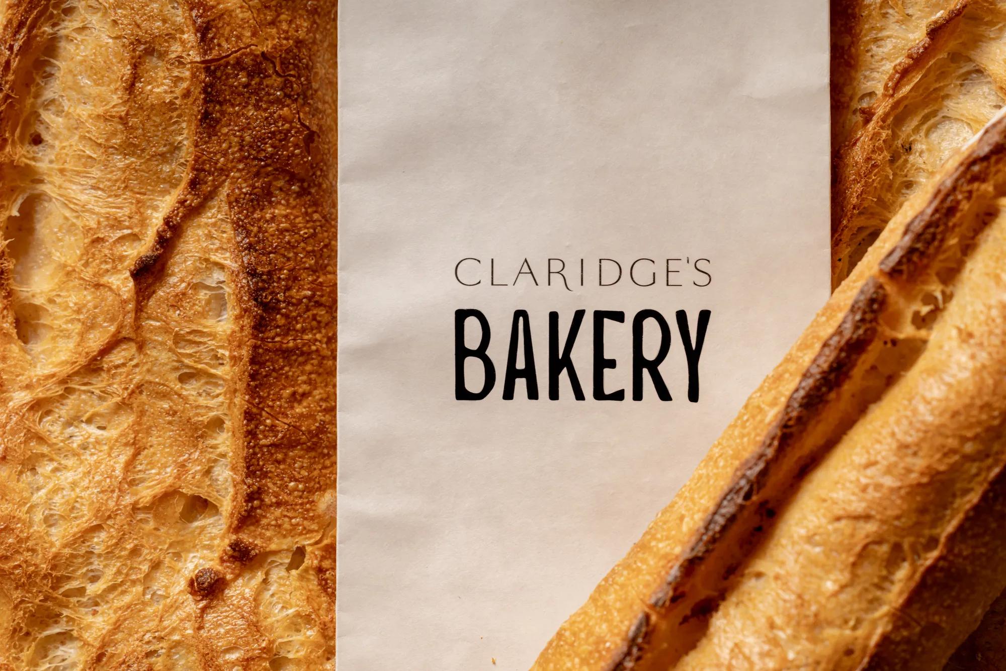Claridge’s Bakery paper bag between crusty baguettes and sliced bread, showing golden texture and branding.