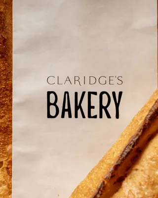 Claridge’s Bakery paper bag between crusty baguettes and sliced bread, showing golden texture and branding.