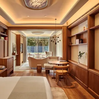 Warm wood-panelled suite with bed, desk and shelving, opening to a sitting area and balcony overlooking gardens.
