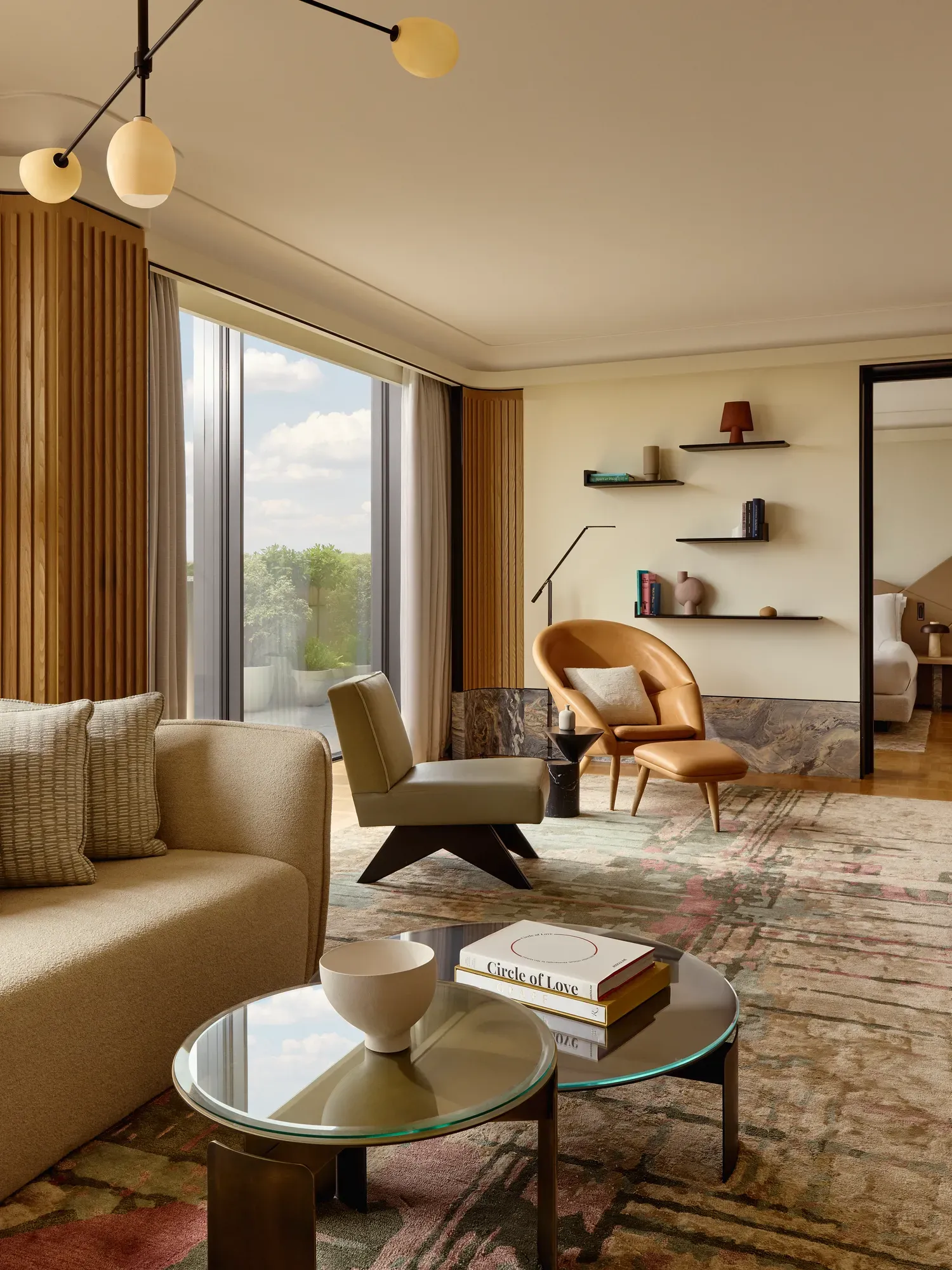 Spacious living room with a cream sofa, leather armchair, and designer lighting, set beside floor-to-ceiling windows overlooking Hyde Park.