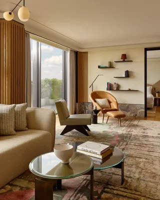Spacious living room with a cream sofa, leather armchair, and designer lighting, set beside floor-to-ceiling windows overlooking Hyde Park.
