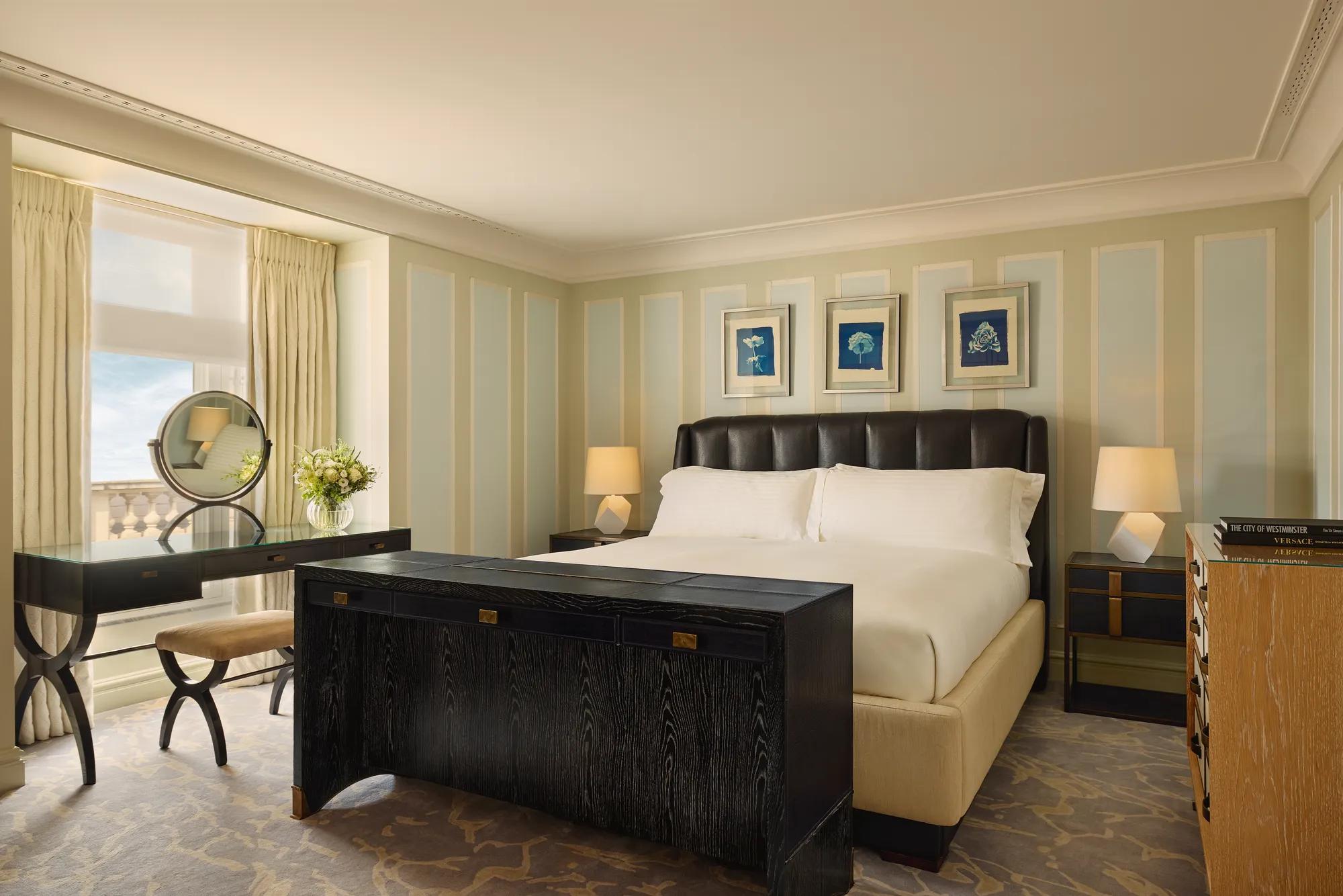 Refined bedroom with leather headboard, black desk and dresser, pastel walls, and artwork above the bed.