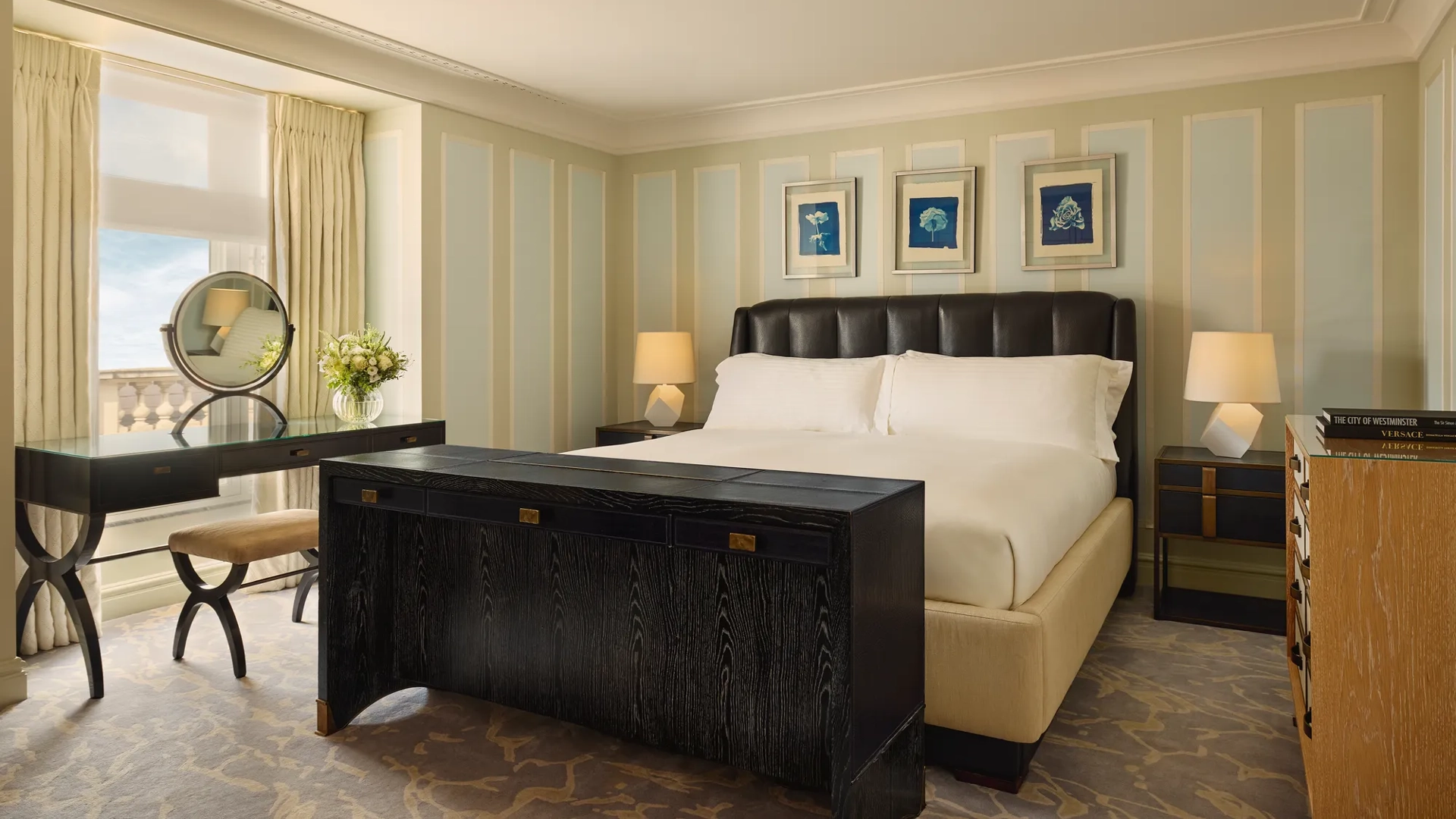 Refined bedroom with leather headboard, black desk and dresser, pastel walls, and artwork above the bed.