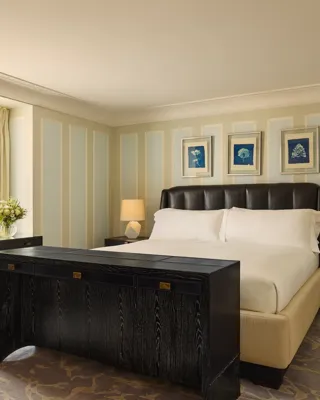Refined bedroom with leather headboard, black desk and dresser, pastel walls, and artwork above the bed.