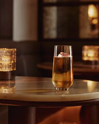 Tall highball with clear ice and citrus slice on a marble table in a dim lounge.