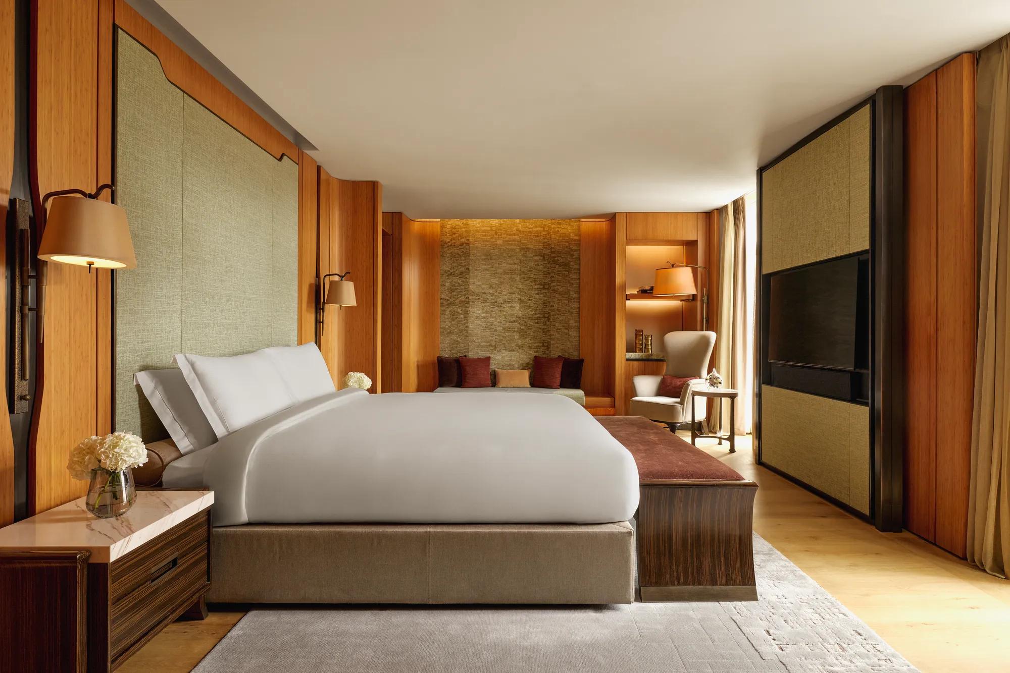 Opus Suite bedroom with king bed, warm wood panelling, lounge seating, and soft lighting