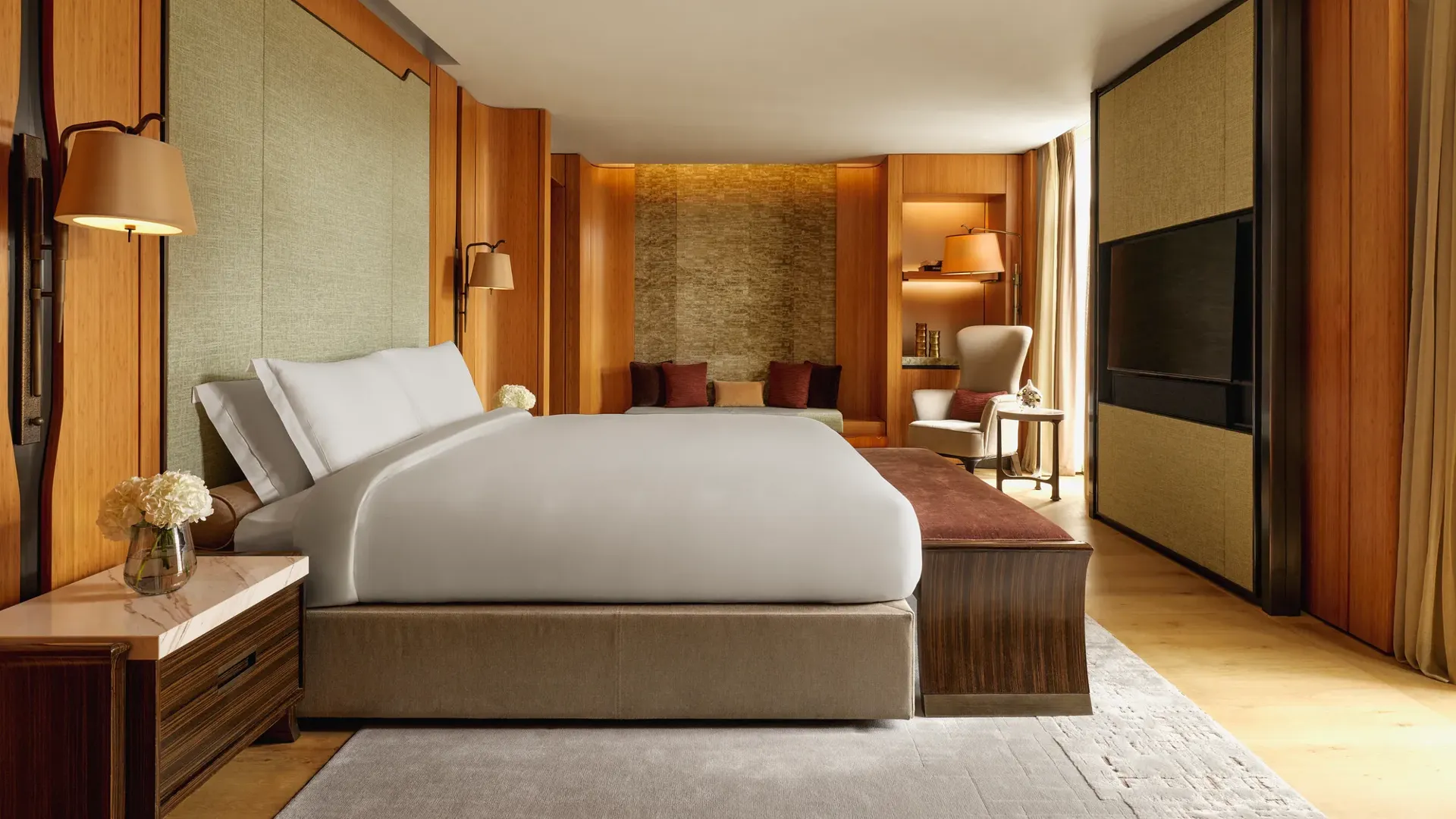 Opus Suite bedroom with king bed, warm wood panelling, lounge seating, and soft lighting