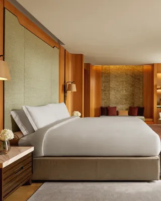 Opus Suite bedroom with king bed, warm wood panelling, lounge seating, and soft lighting