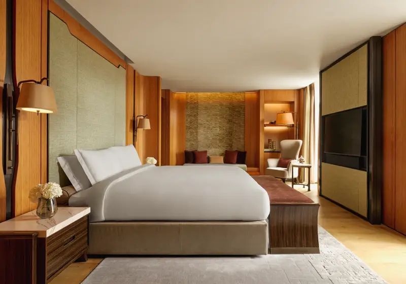 Opus Suite bedroom with king bed, warm wood panelling, lounge seating, and soft lighting