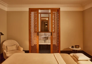 Tranquil spa room with a treatment bed, soft armchair, and carved wooden screens revealing a small sink area.
