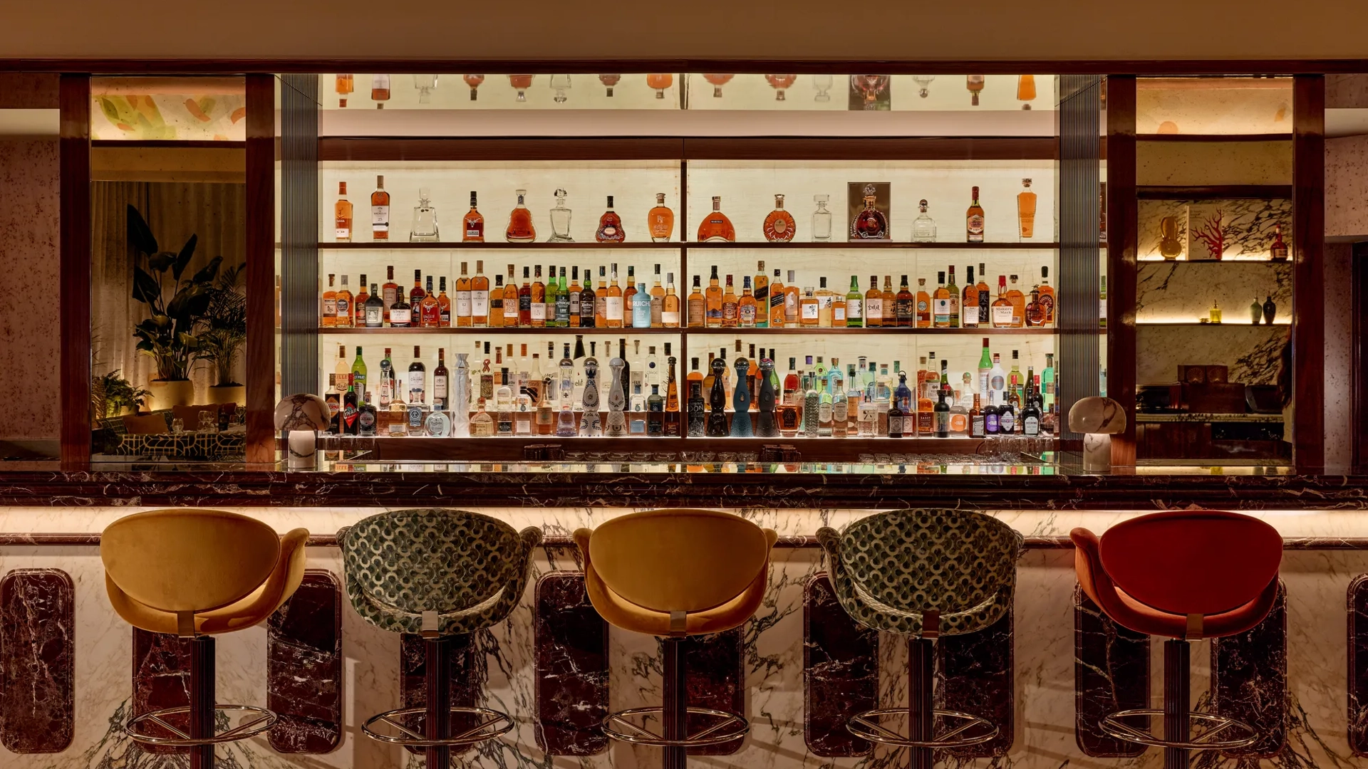 Well-stocked bar with marble counter and five upholstered bar stools in warm, ambient lighting.
