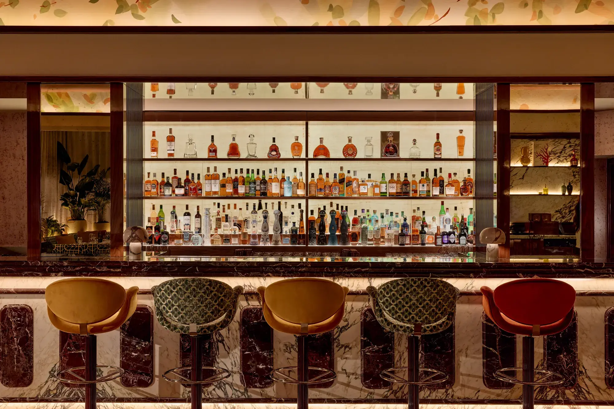 Well-stocked bar with marble counter and five upholstered bar stools in warm, ambient lighting.