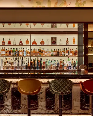 Well-stocked bar with marble counter and five upholstered bar stools in warm, ambient lighting.