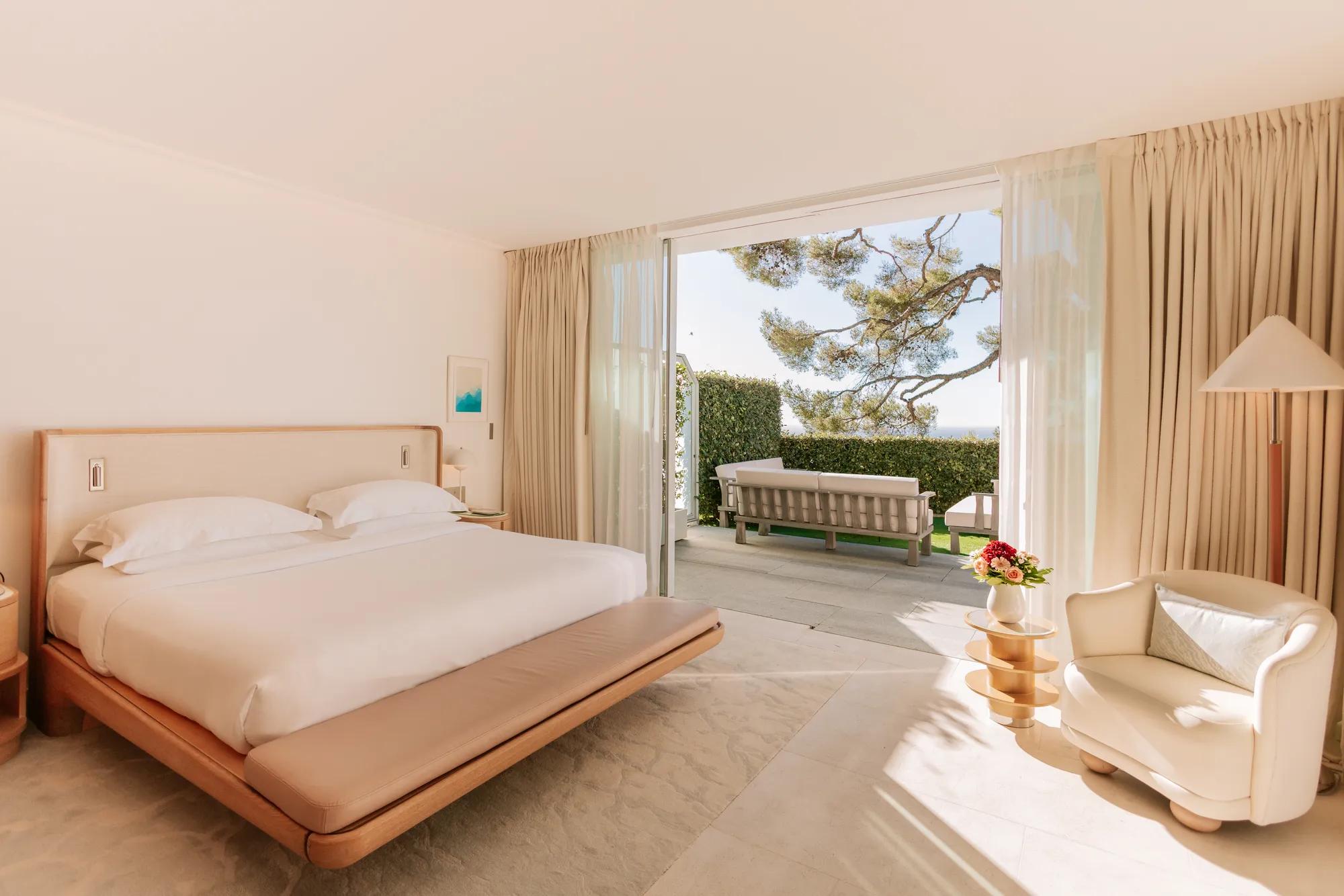 Bright bedroom with king bed and seating area opening onto a private terrace with sea view.