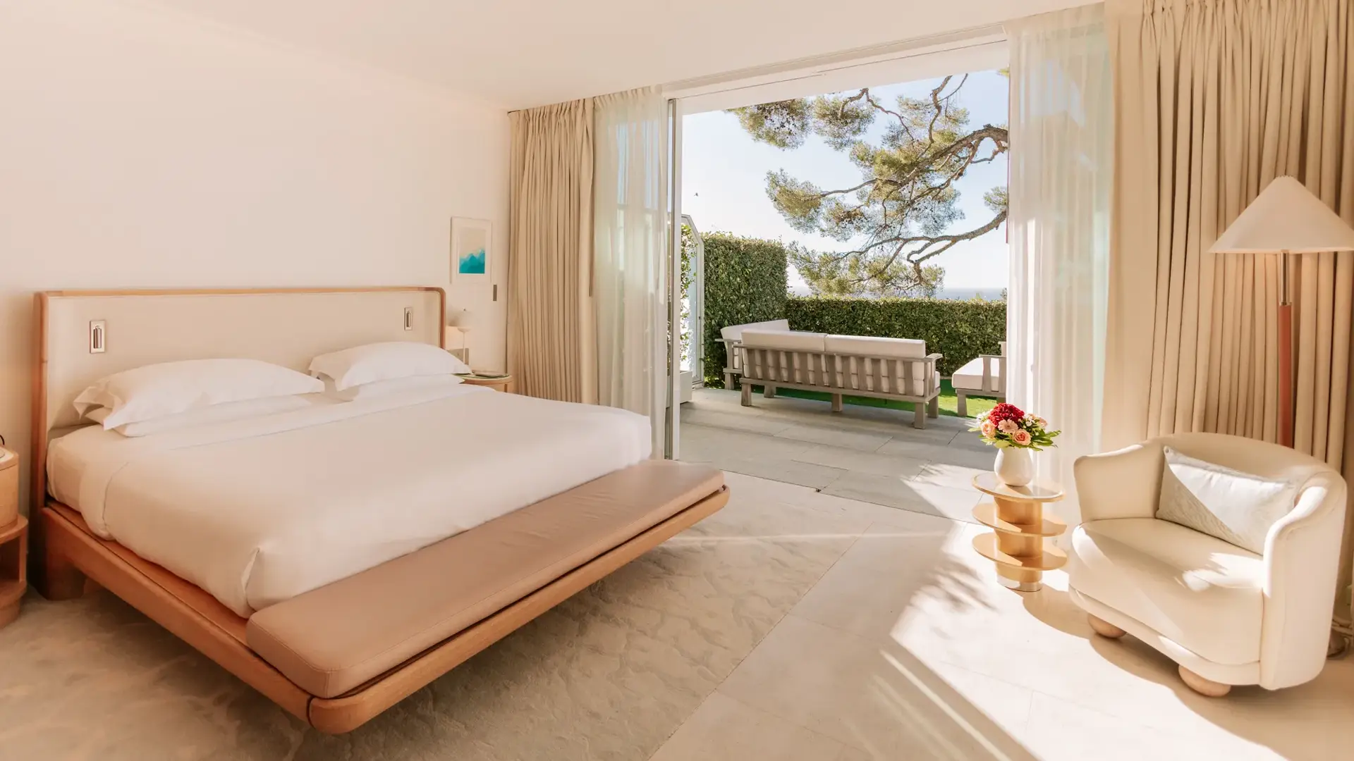 Bright bedroom with king bed and seating area opening onto a private terrace with sea view.