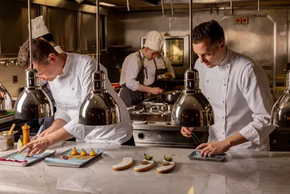 Chefs in a professional kitchen carefully plating dishes under heat lamps.