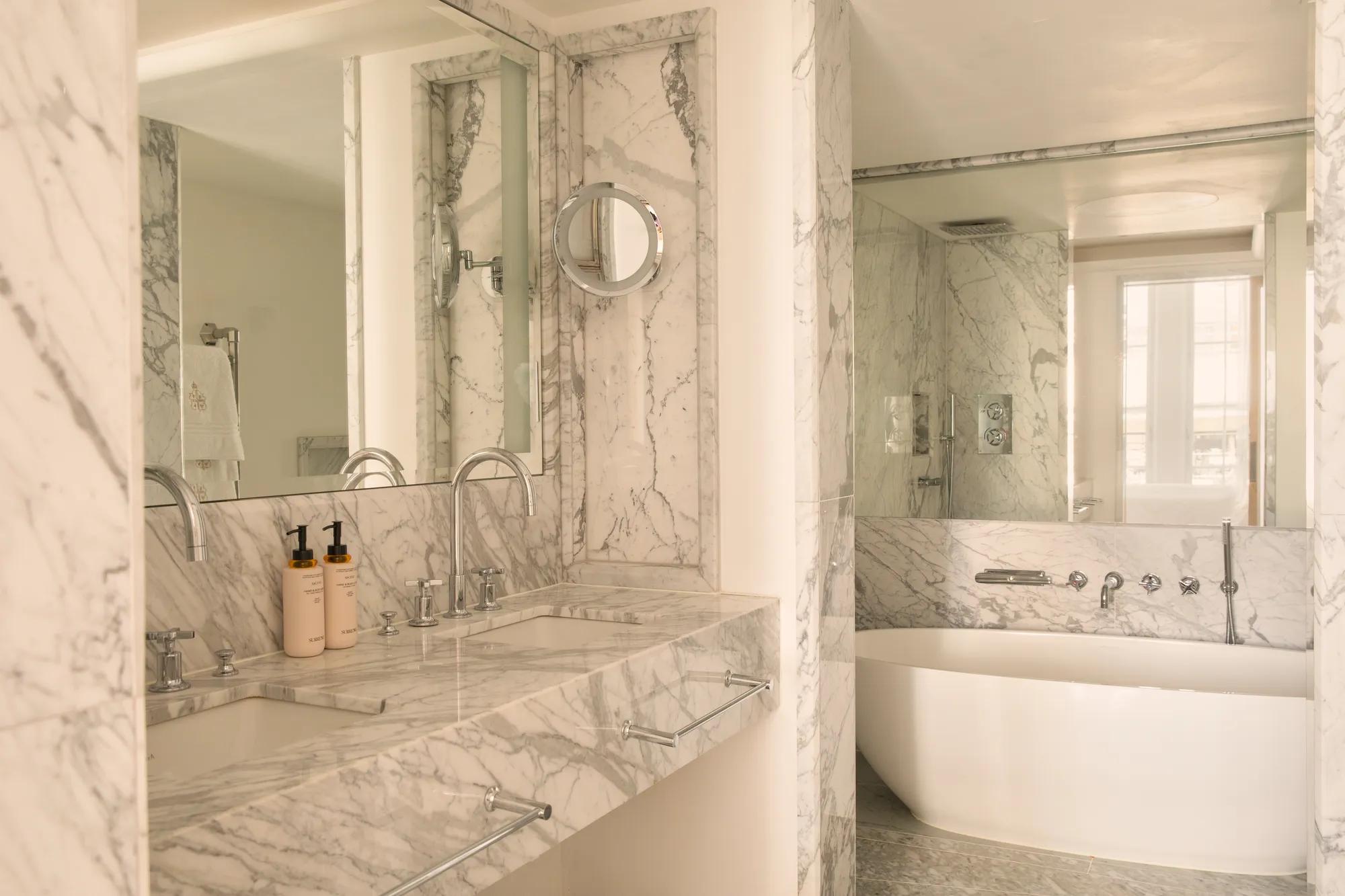 Elegant marble bathroom with a double vanity, freestanding bath and walk-in shower, bathed in soft natural light.
