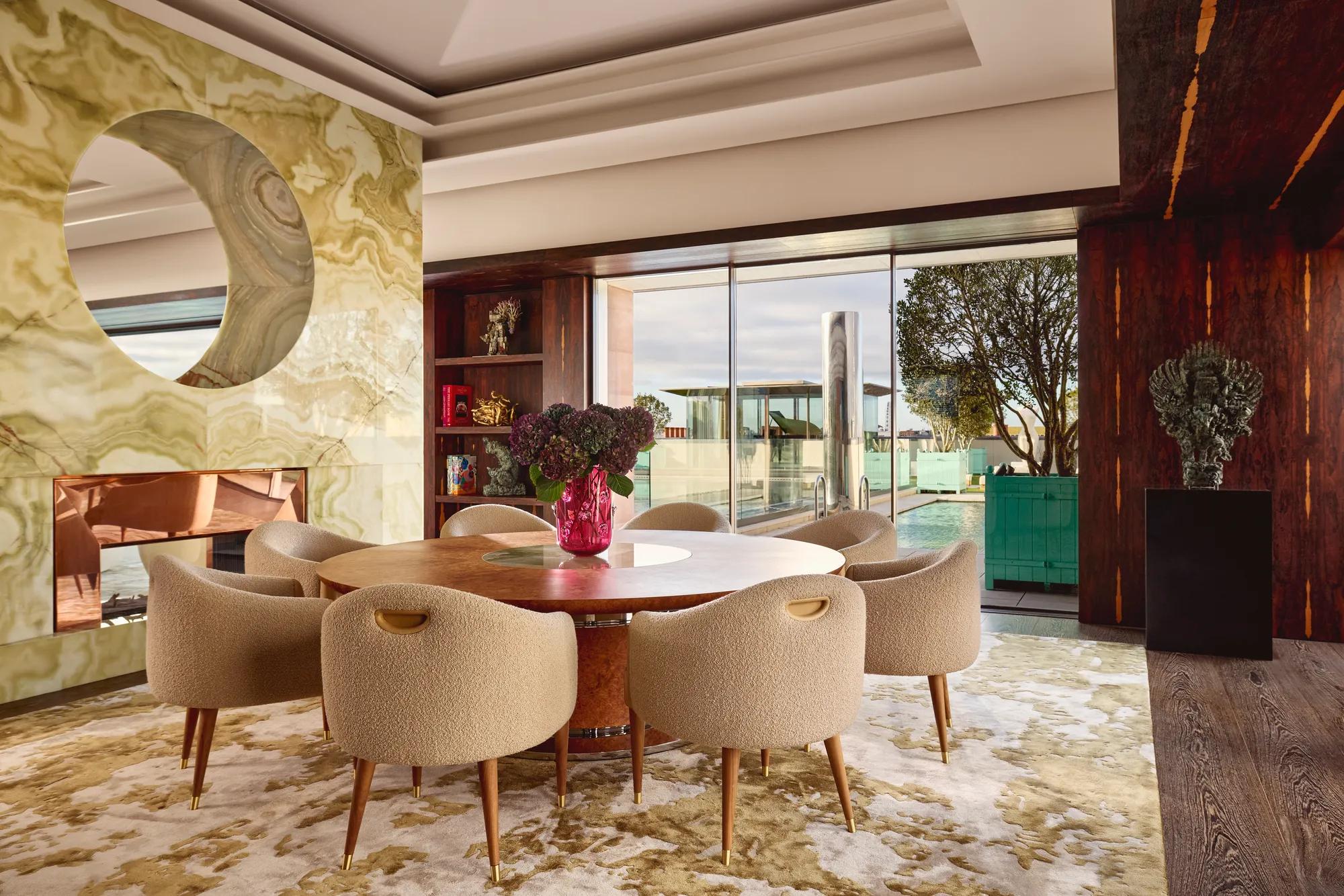 Penthouse dining area at Claridge’s with a round wooden table, cream chairs, and glass doors opening onto a rooftop terrace.