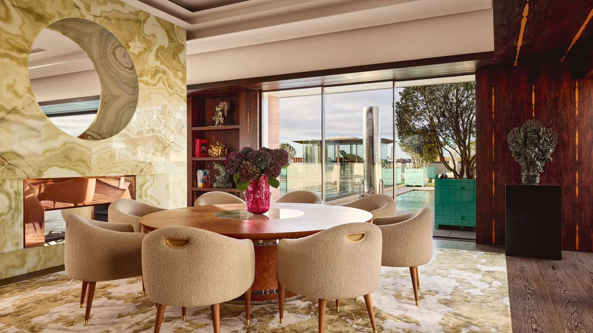 Penthouse dining area at Claridge’s with a round wooden table, cream chairs, and glass doors opening onto a rooftop terrace.