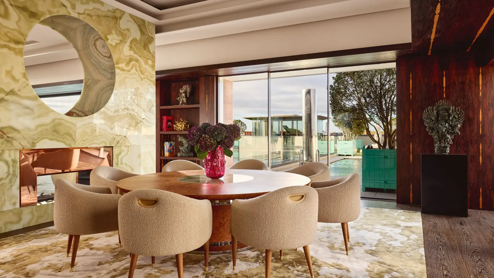 Penthouse dining area at Claridge’s with a round wooden table, cream chairs, and glass doors opening onto a rooftop terrace.