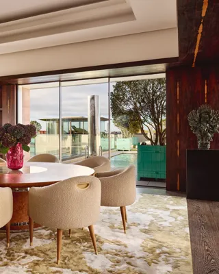 Penthouse dining area at Claridge’s with a round wooden table, cream chairs, and glass doors opening onto a rooftop terrace.