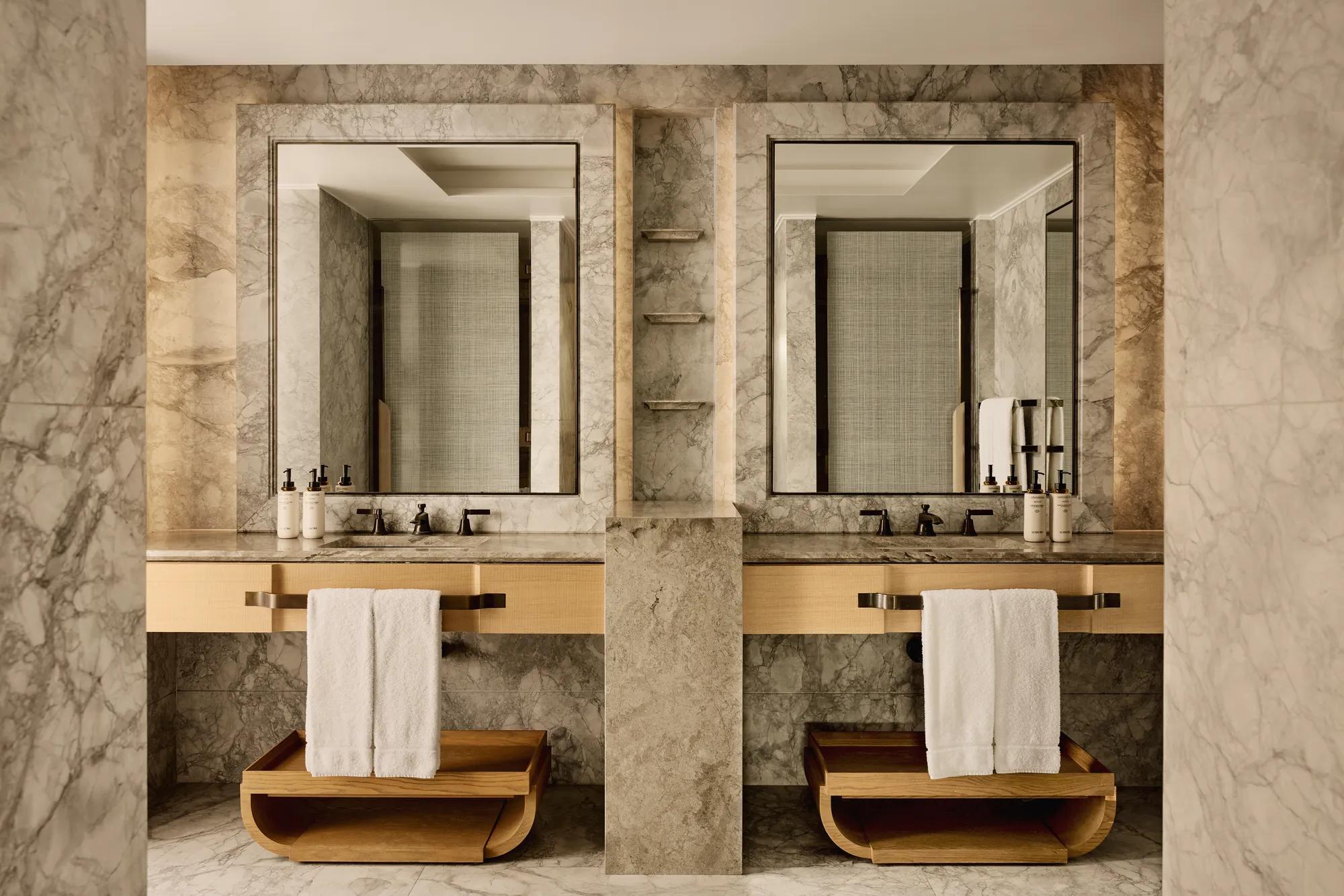 Bathroom with marble walls, dual sinks, large mirrors, and wooden towel shelves beneath counters