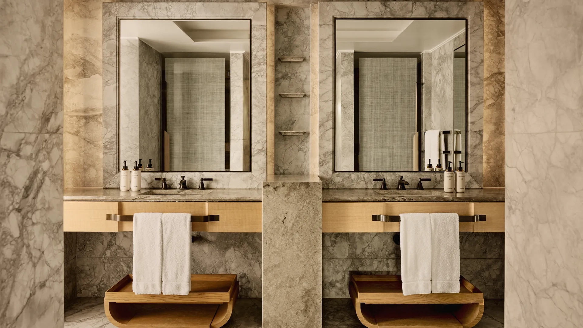 Bathroom with marble walls, dual sinks, large mirrors, and wooden towel shelves beneath counters