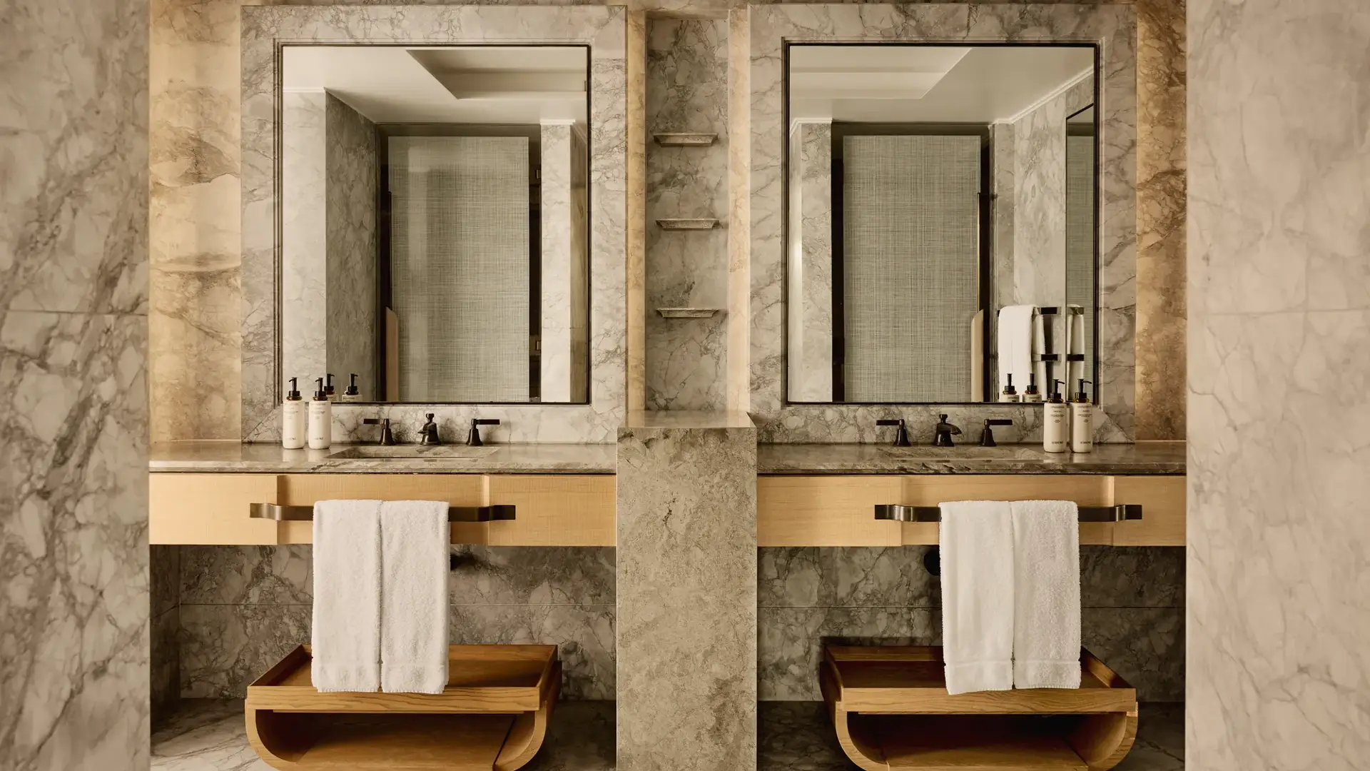 Bathroom with marble walls, dual sinks, large mirrors, and wooden towel shelves beneath counters