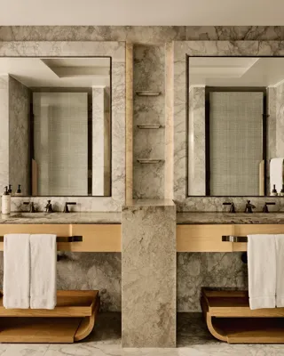 Bathroom with marble walls, dual sinks, large mirrors, and wooden towel shelves beneath counters