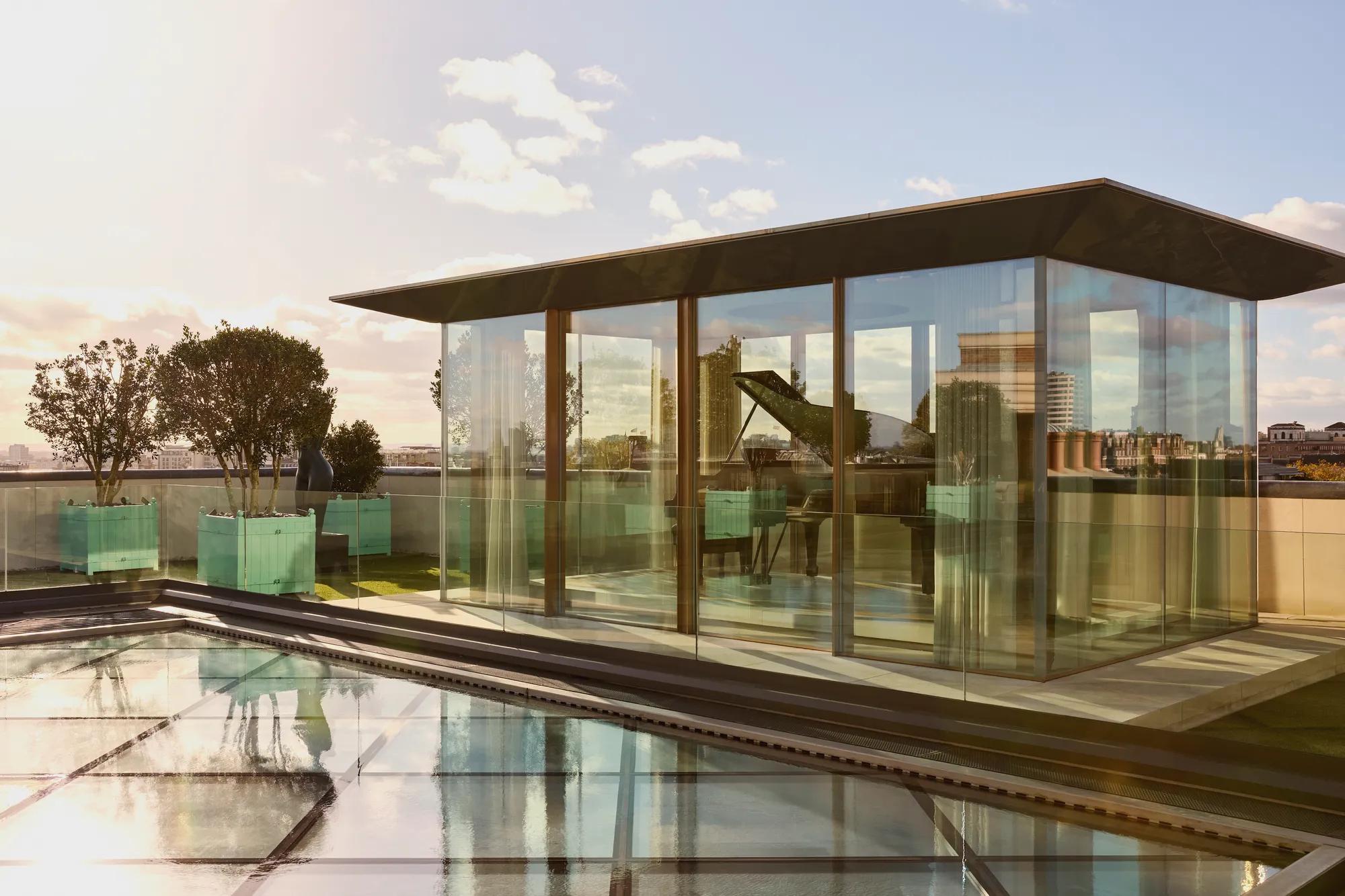Rooftop glass pavilion at Claridge’s with a grand piano inside, surrounded by planters and views across London.