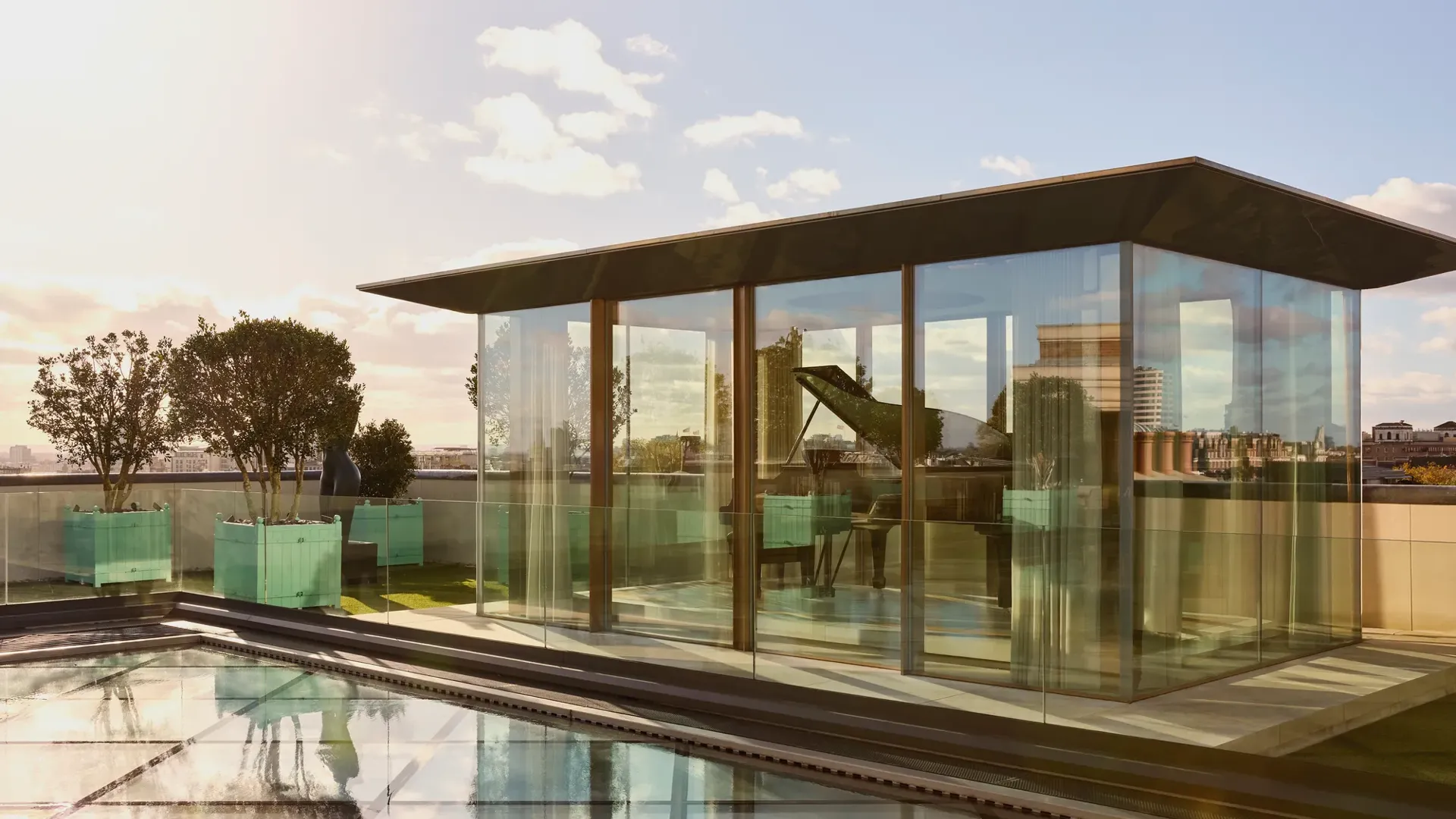Rooftop glass pavilion at Claridge’s with a grand piano inside, surrounded by planters and views across London.