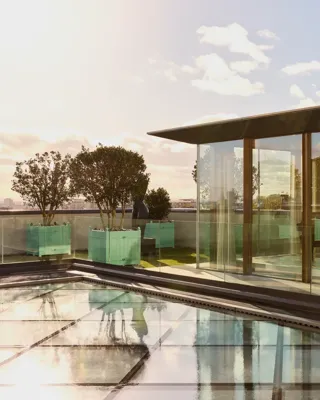 Rooftop glass pavilion at Claridge’s with a grand piano inside, surrounded by planters and views across London.