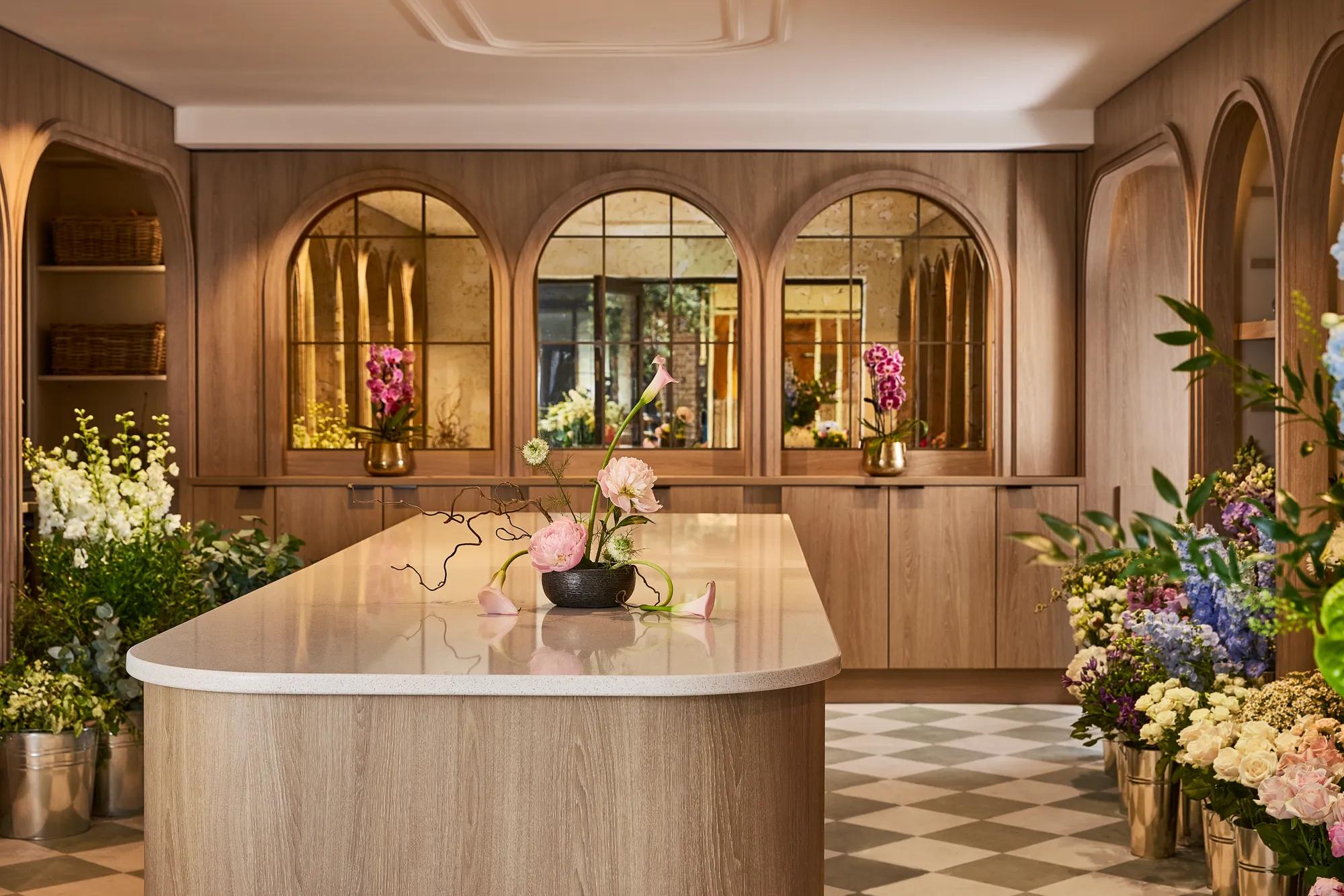 Central display table with a floral arrangement, surrounded by fresh flowers, warm oak panelling and arched mirrored alcoves.